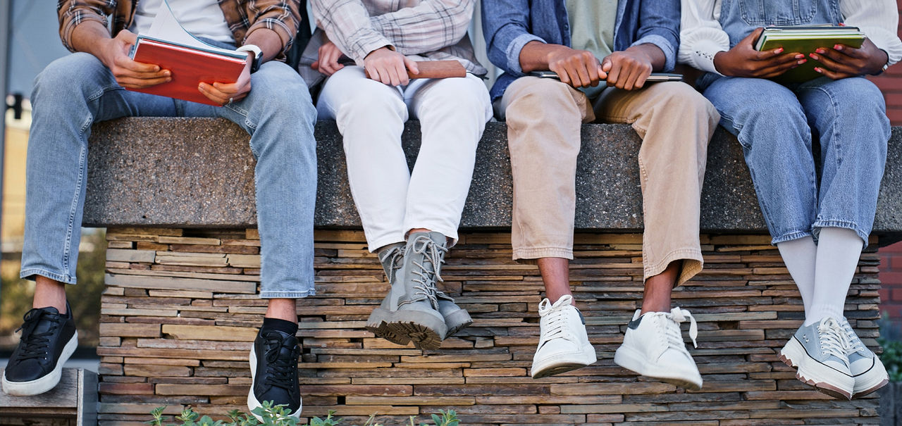 Feet, students and wall with book at school for education, learning support and studying of growth development. People, legs and rest for knowledge, university and reading for morning information